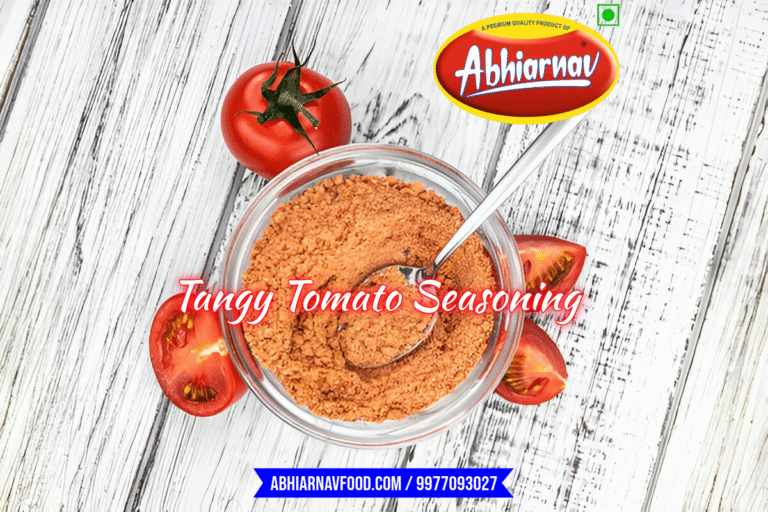 Abhiarnav Tangy Tomato Seasoning in glass bowl with spoon, surrounded by fresh tomatoes – perfect spicy flavor for snacks, chips, and Fryums
